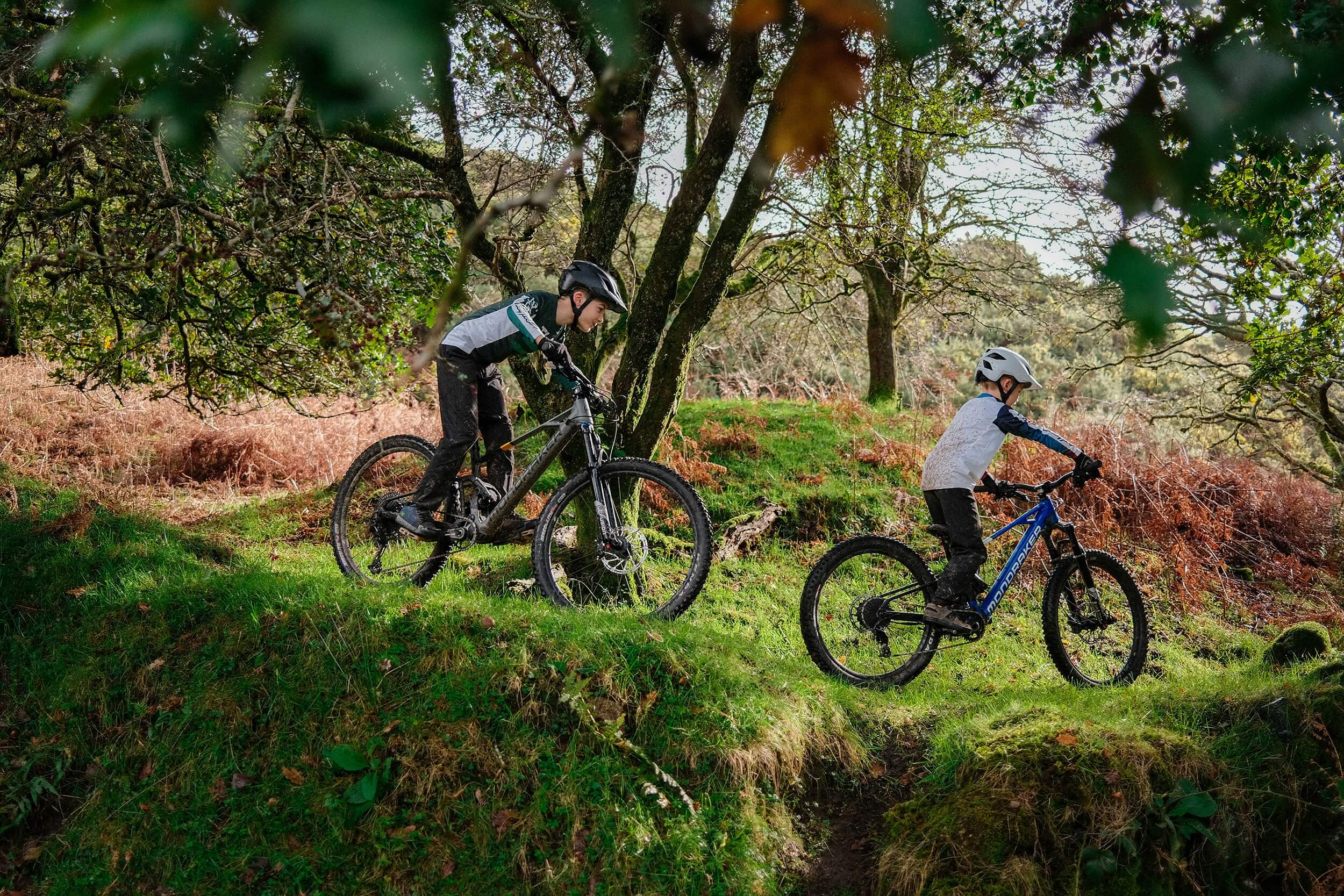 Kinder auf Mondraker-Bikes fahren durch einen bewaldeten Hügel.