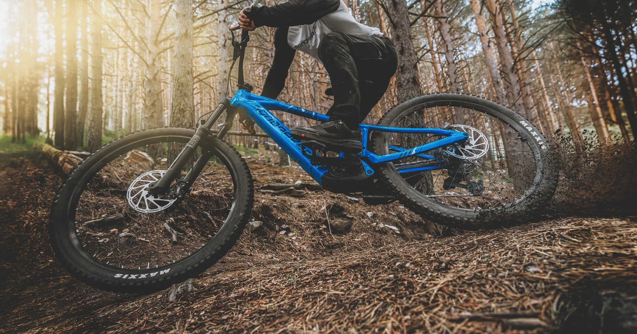 Fahrradfahrer auf einem blauen Mondraker Sly Mountainbike im Wald, geeignet für anspruchsvolle Geländefahrten.