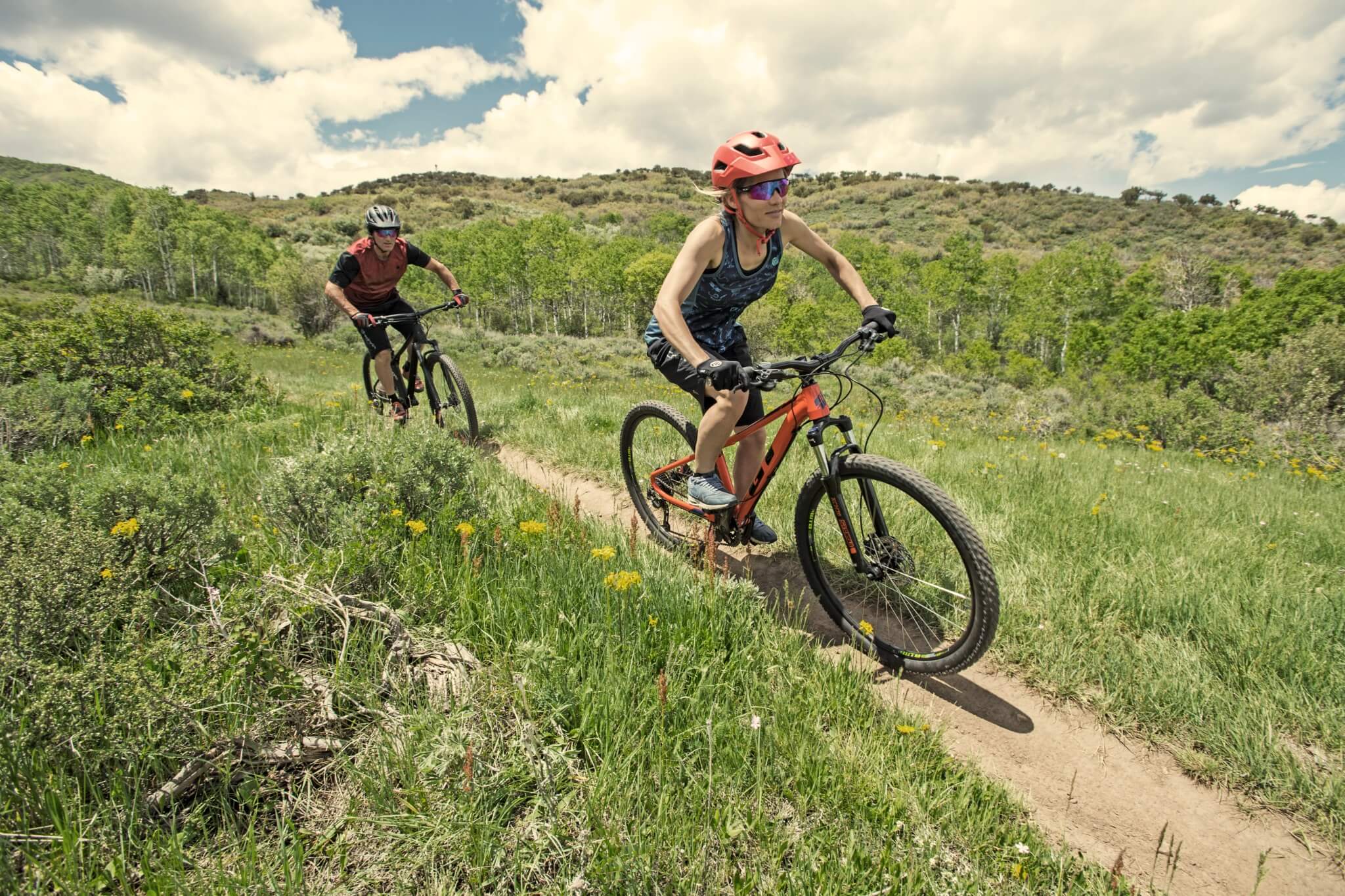 Zwei Personen fahren GT Mountainbikes auf schmalem Pfad durch grüne Landschaft, ideal für Outdoor-Enthusiasten.