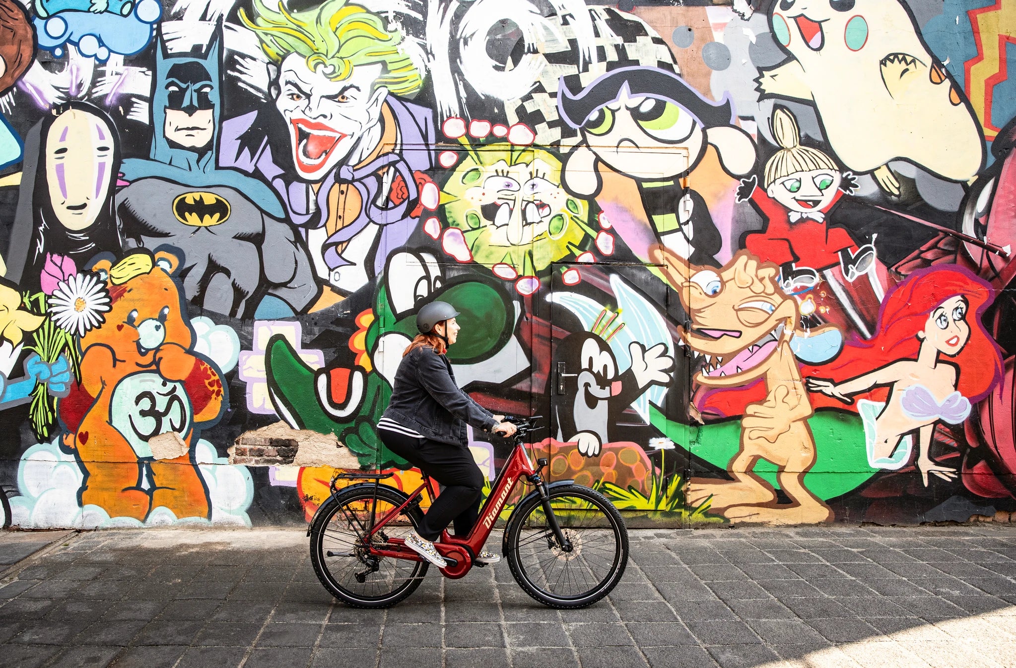 Person auf rotem Diamant-Fahrrad vor bunter Comic-Wand. Ideal für Stadtrundfahrten und urbane Abenteuer.