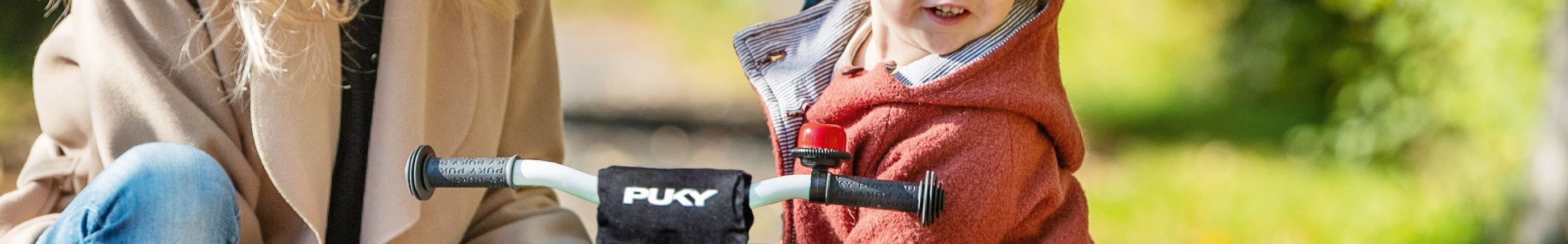 Kind auf Puky-Dreirad zusammen mit Erwachsener im Freien. Ideal für kleine Kinder zum Radfahren lernen.