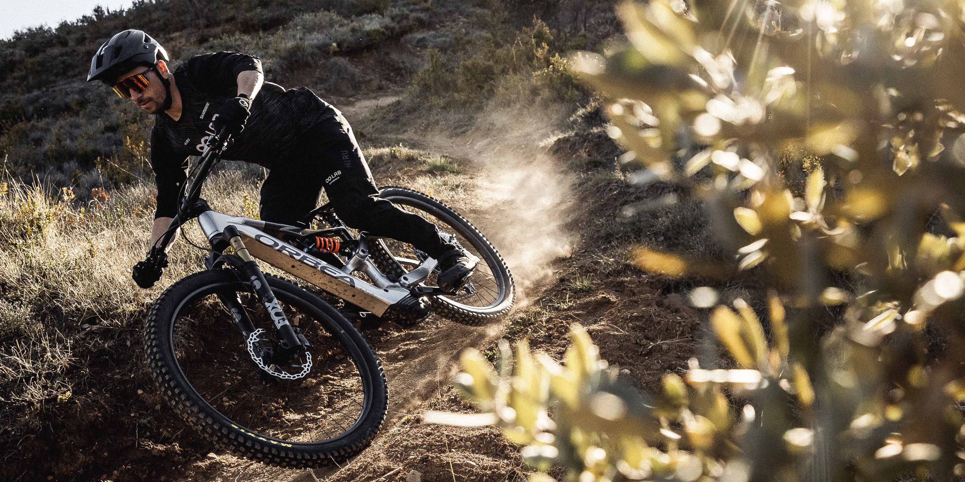 Person fährt mit einem Orbea Mountainbike rasant durch einen kurvigen, staubigen Trail in der Natur.