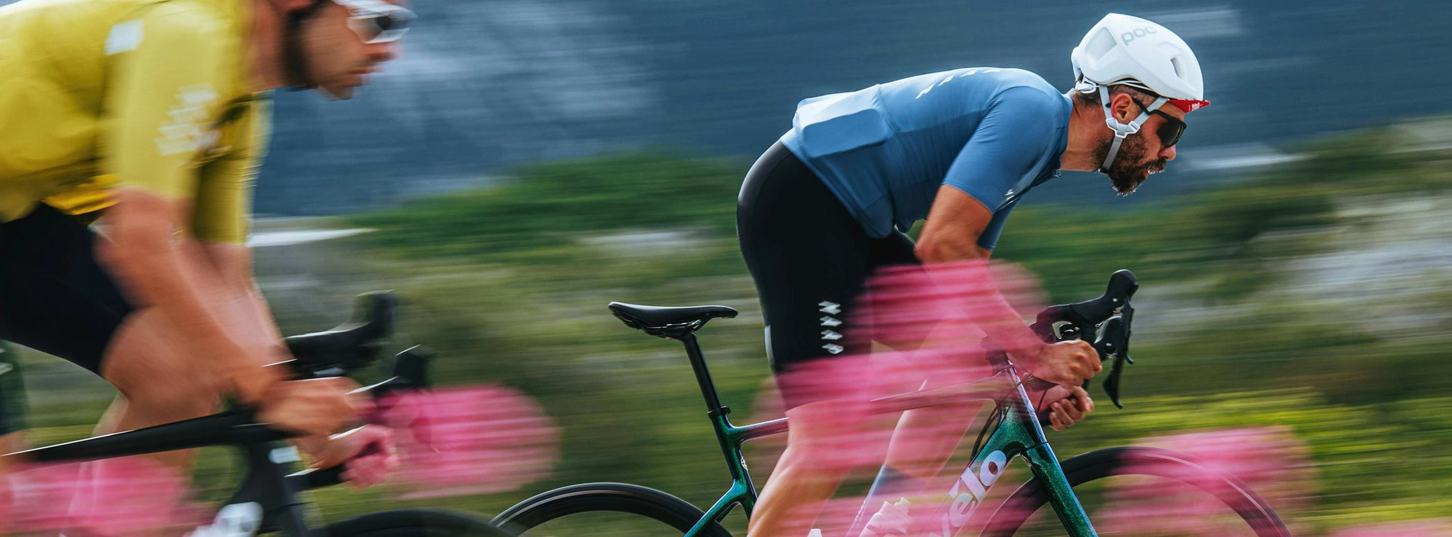 Zwei Radfahrer mit Cervélo-Rädern in Rennposition, düsen durch eine landschaftliche Umgebung.