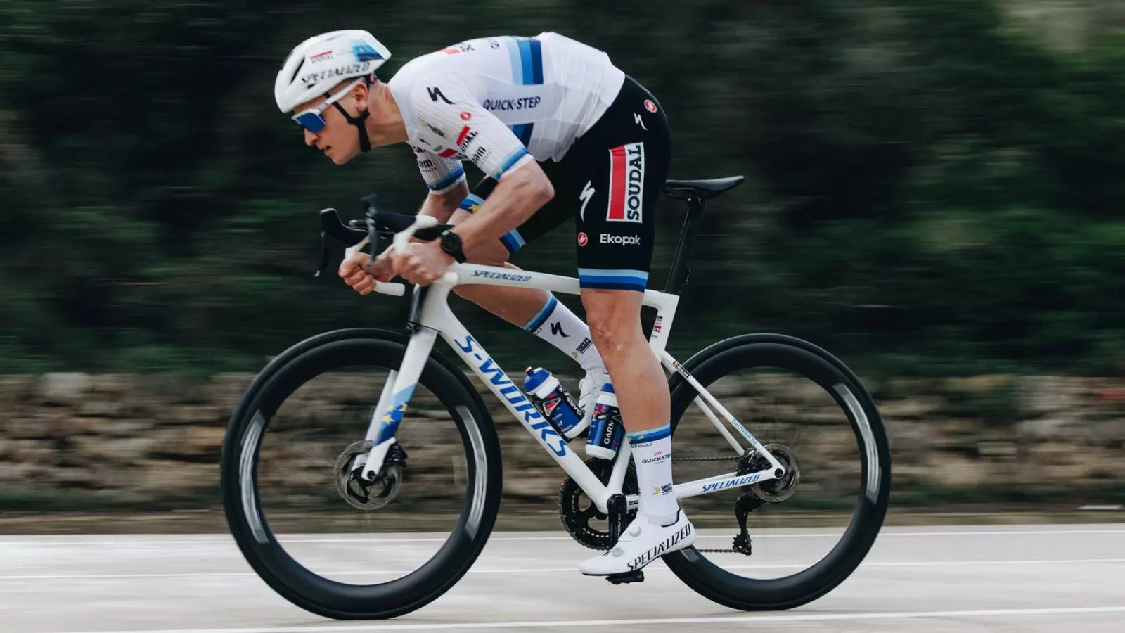 Radfahrer auf Specialized S-Works Rennrad in aerodynamischer Position, mit Teamkleidung und Helm auf offener Straße.