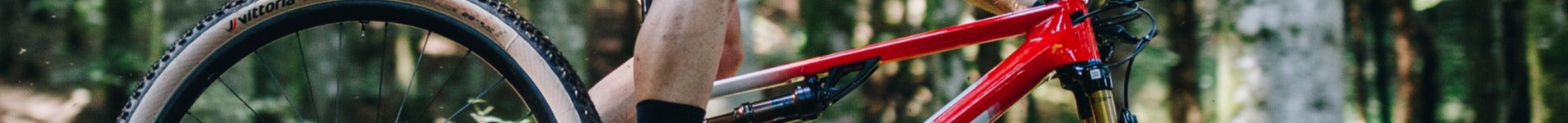 Rotes BMC Fourstroke Mountainbike im Wald, seitliche Nahaufnahme, Schwerpunkt auf Rahmen und Vorderrad.