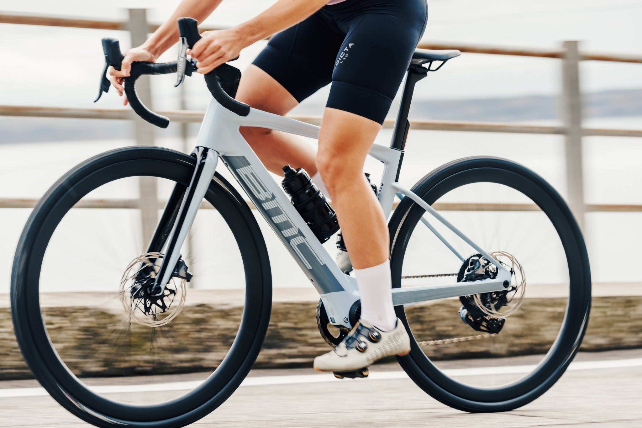 Person auf einem BMC-Rennrad bei einer Fahrt entlang der Küste auf einem hölzernen Weg.