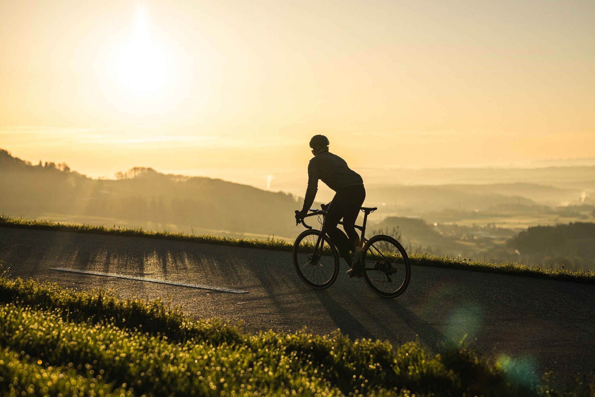 Radfahrer im Sonnenuntergang auf Landstraße. Perfekt für Rennradbegeisterte. BMC-Rennrad, geeignet für sportliche Touren.