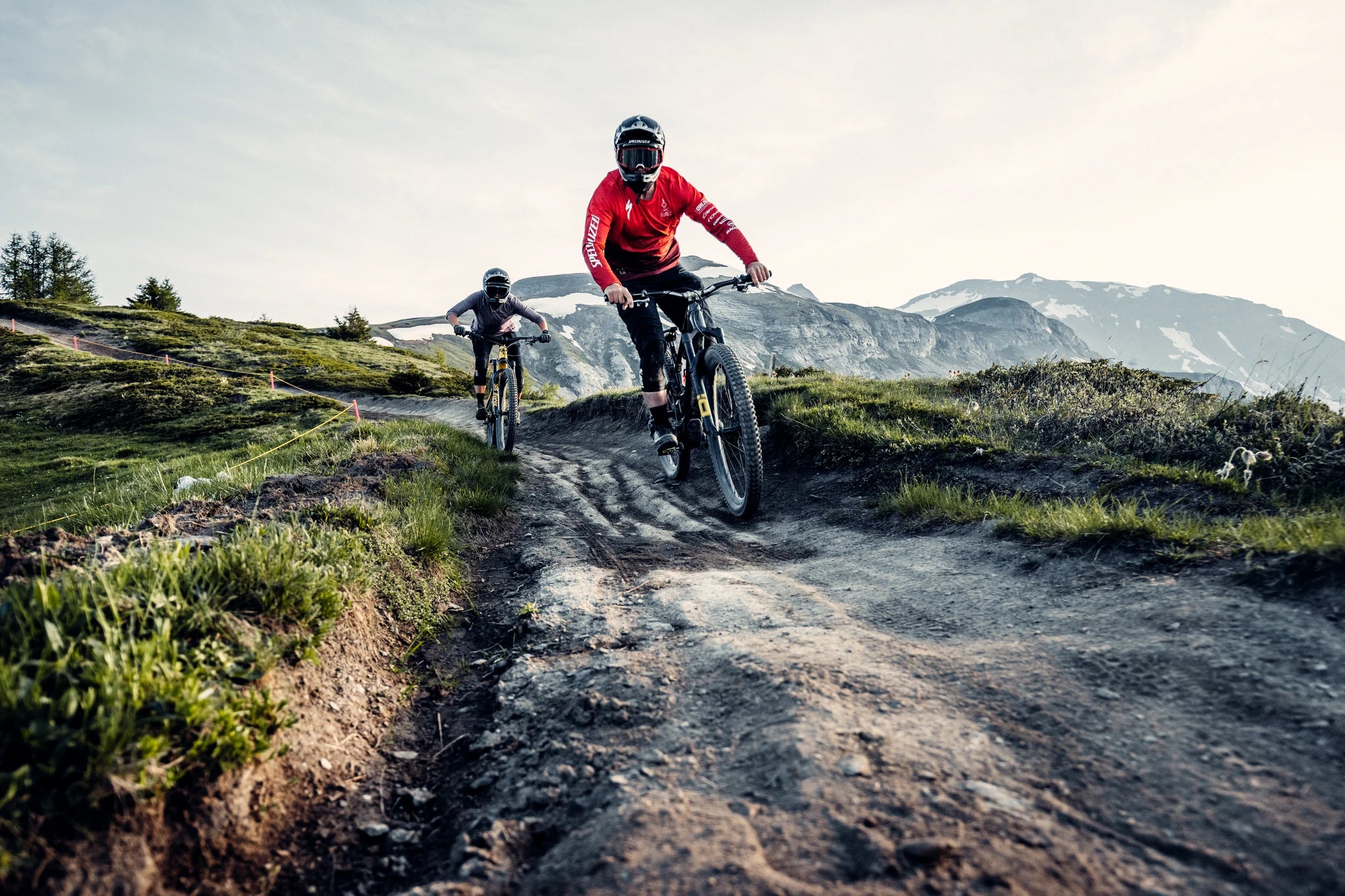 Zwei Mountainbiker fahren auf einem schmalen Weg bergab. Specialized S-Works Fahrrad erkennbar.