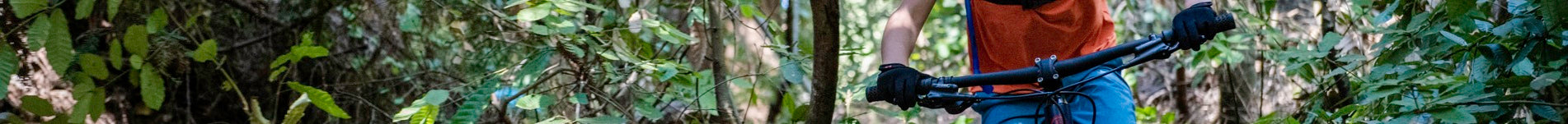 Person auf Mountainbike im Wald, trägt rote Weste und blaue Hose. Ideal für Outdoor-Abenteuer und sportliche Aktivität.