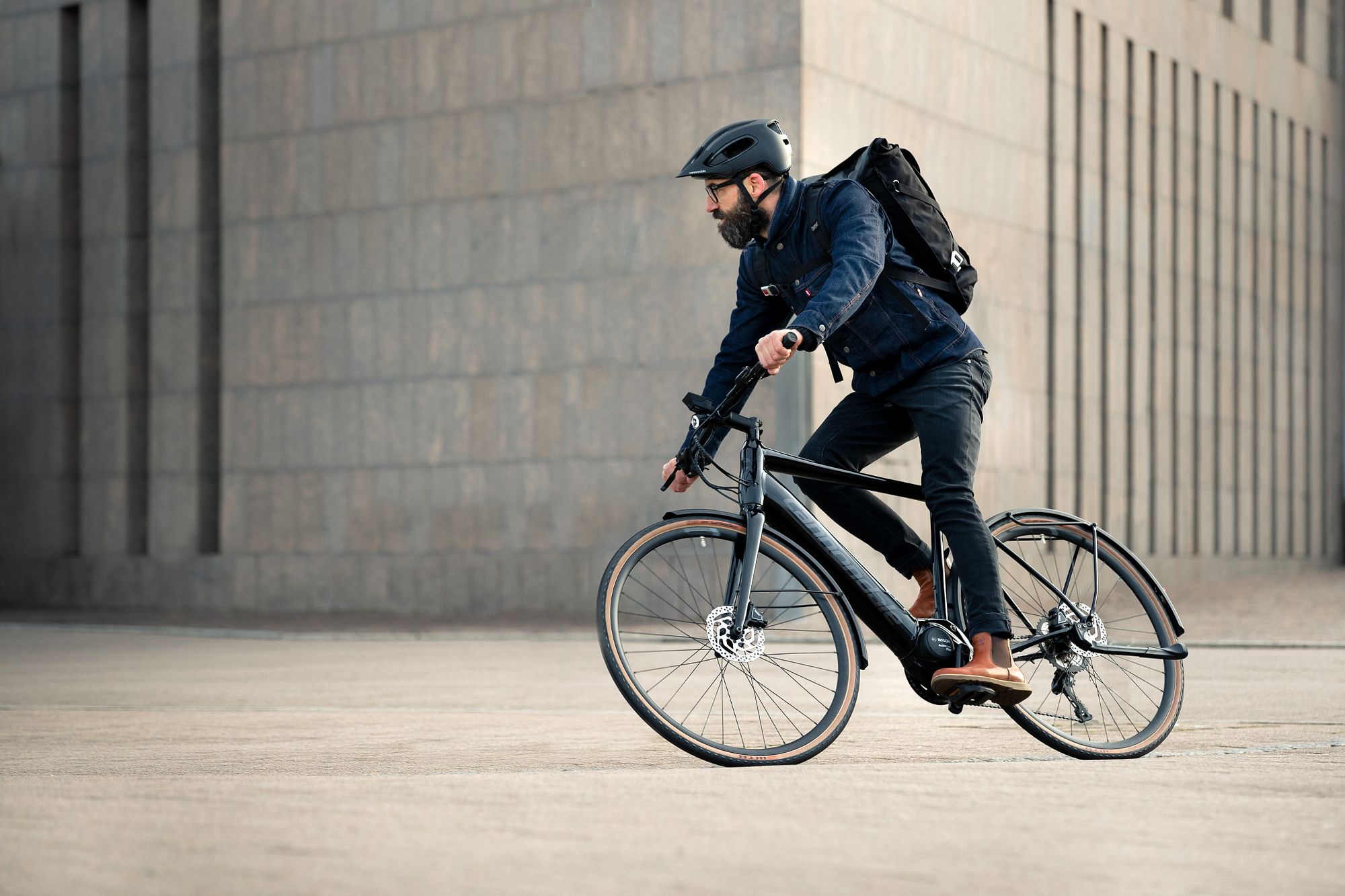 Mann fährt auf einem Cannondale E-City Urban Bike in urbaner Umgebung, mit Helm und Rucksack.