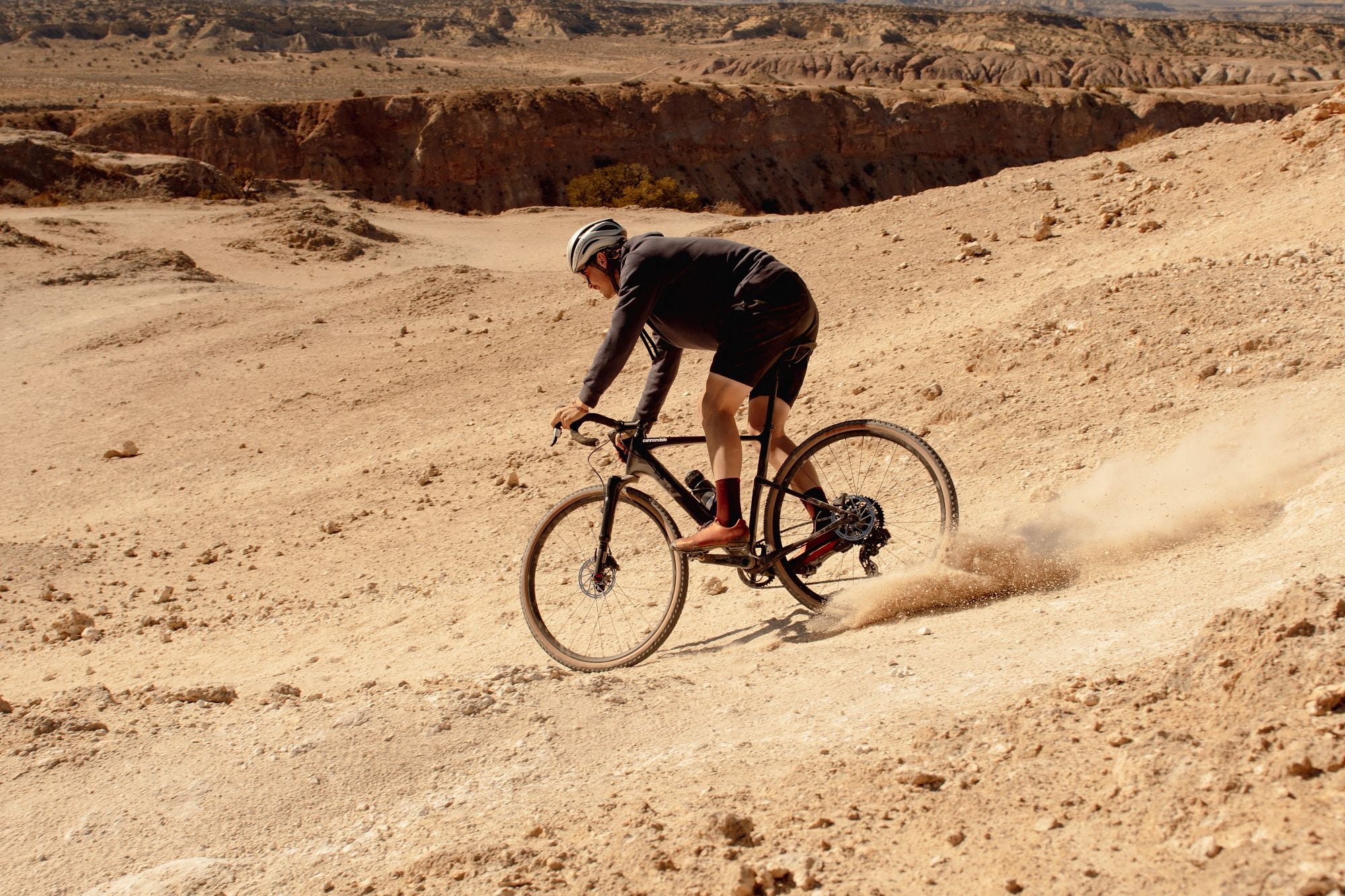 Fahrradfahrer auf Cannondale SuperX in Wüstenlandschaft beim Downhill. Offroad-Cyclocross für Abenteurer.