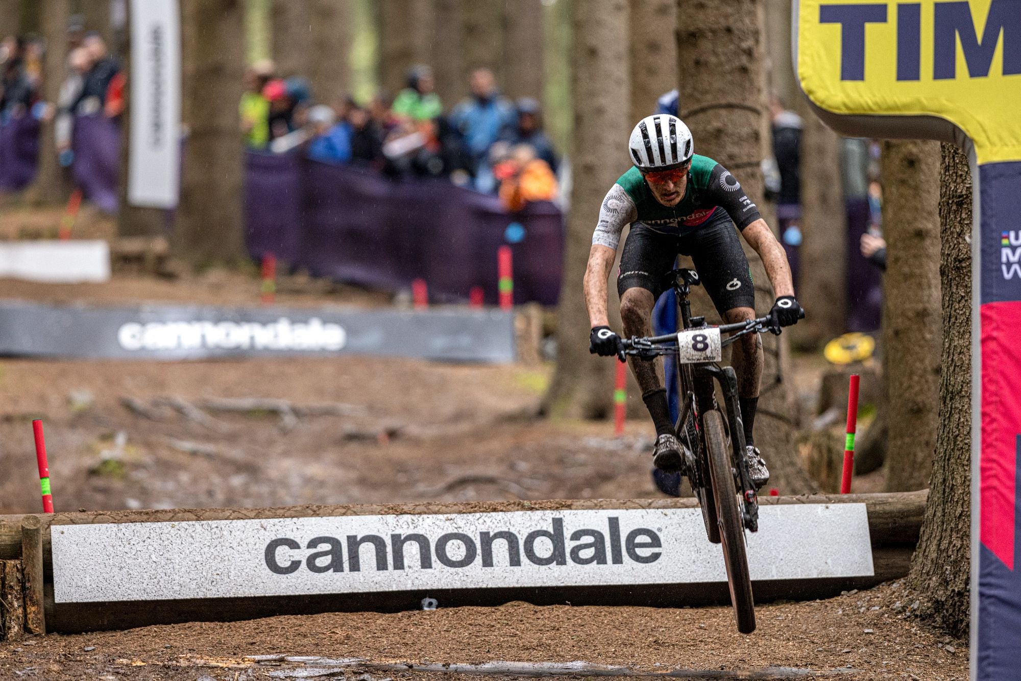 Radfahrer auf einem Cannondale Scalpel Mountainbike bei einem Rennen im Wald, Zuschauer im Hintergrund.