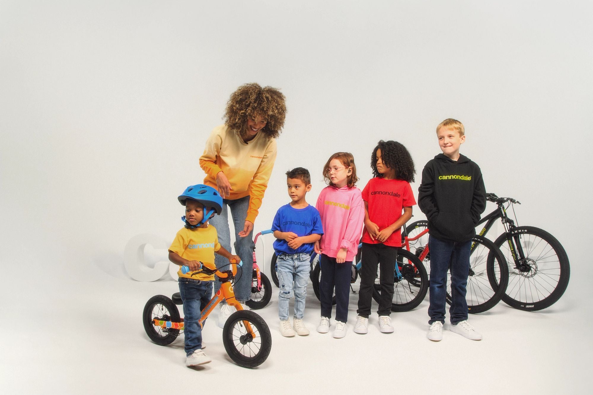 Kinder in Cannondale-Kleidung mit Fahrrädern, ein Kind auf Laufrad mit Helm, geeignet für junge Radfahrer.