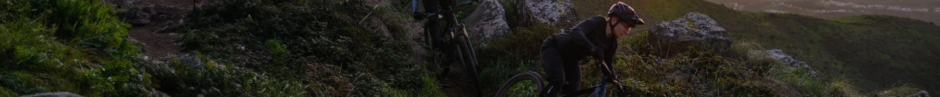 Mountainbiker fährt auf einem Pfad zwischen Felsen und Gras mit einem Cube-MTB.