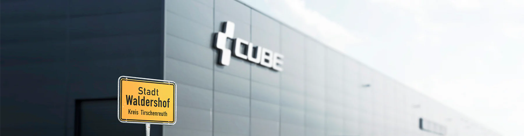 Gelbes Ortsschild von Waldernhof vor einem modernen Gebäude mit dem Logo von Cube.