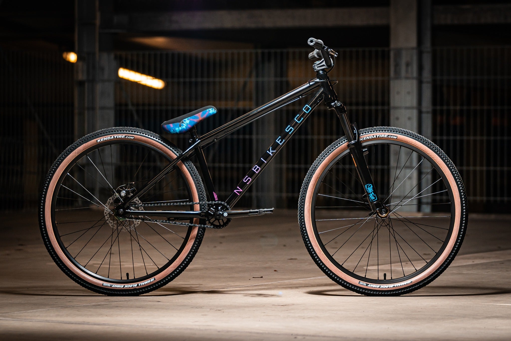 Schwarzes NS Bikes BMX-Rad mit farbigem Sattel in Tiefgarage, geeignet für Tricks und Sprünge, Reifen von Kenda.