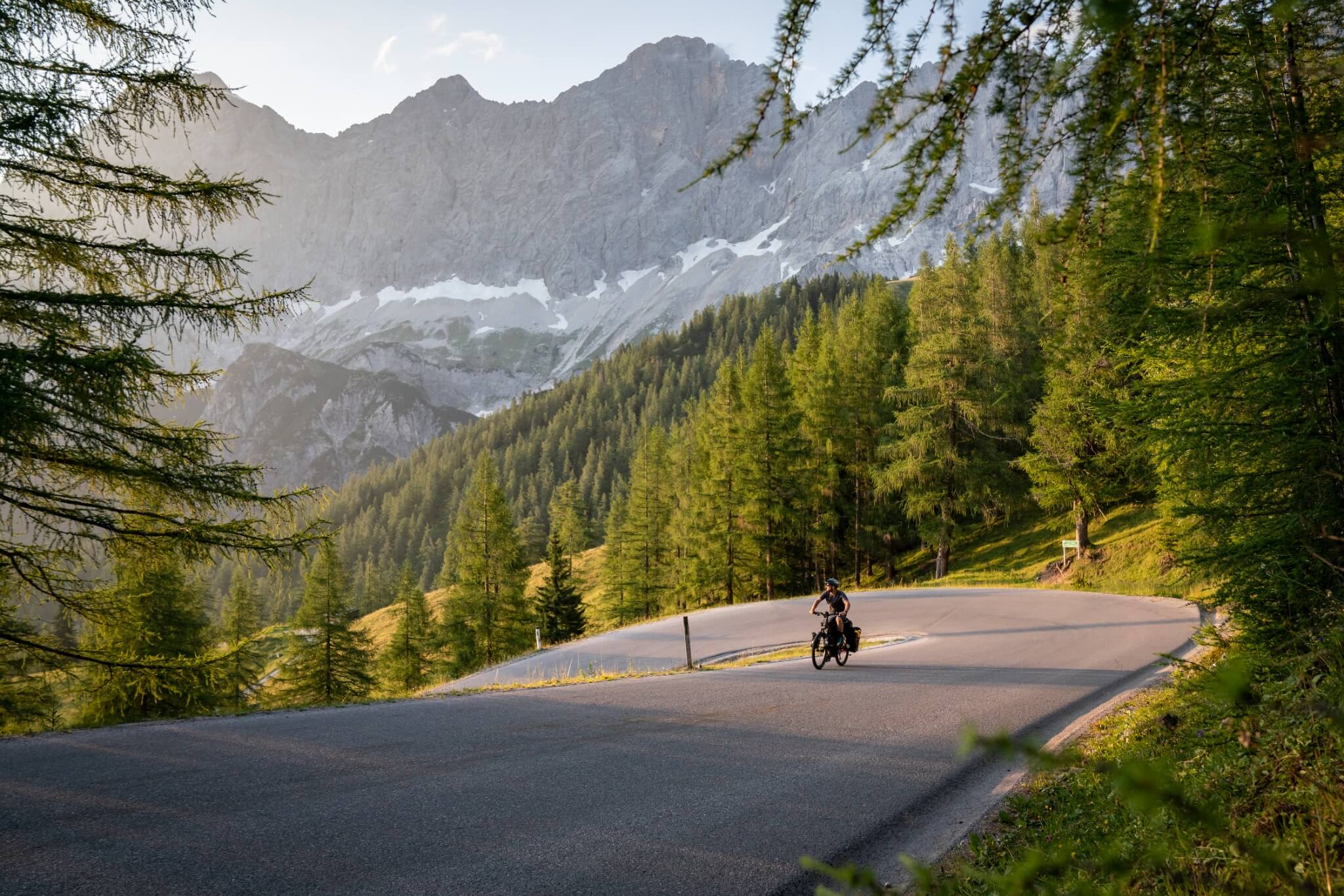 Person fährt Haibike E-Bike auf einer kurvigen Bergstraße, umgeben von Wald und Bergen, ideal für Outdoor-Enthusiasten.
