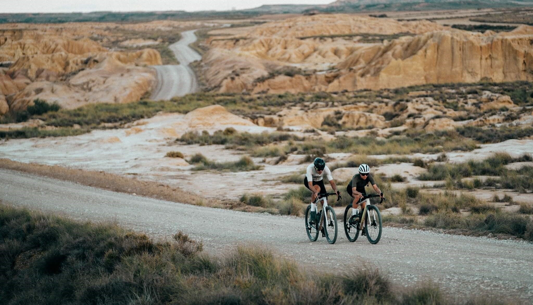 Zwei Radfahrer auf Schotterstraße in Wüstenlandschaft. Ideal für Gravelbiking-Enthusiasten.