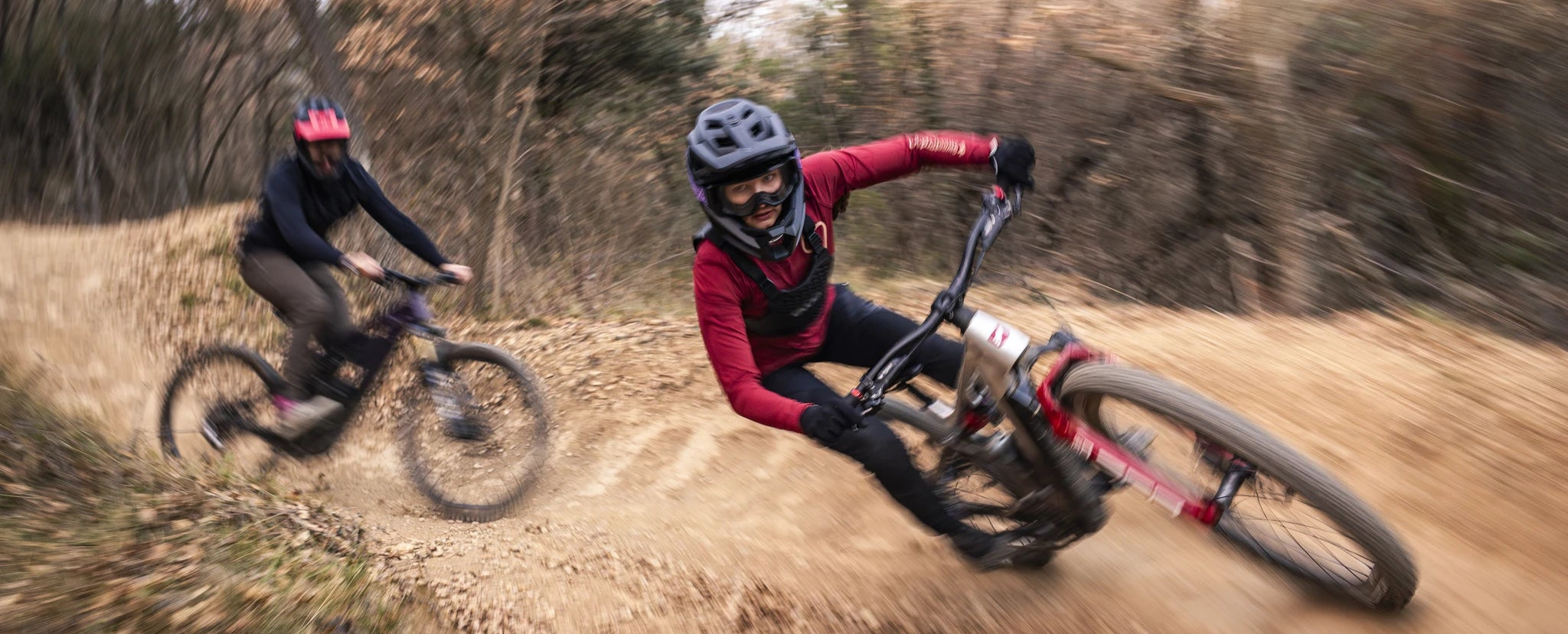 Zwei Personen auf E-Mountainbikes im Drift auf schlammiger Strecke, Fokus SAM² Modell, sportliche Outdoor-Aktivität.