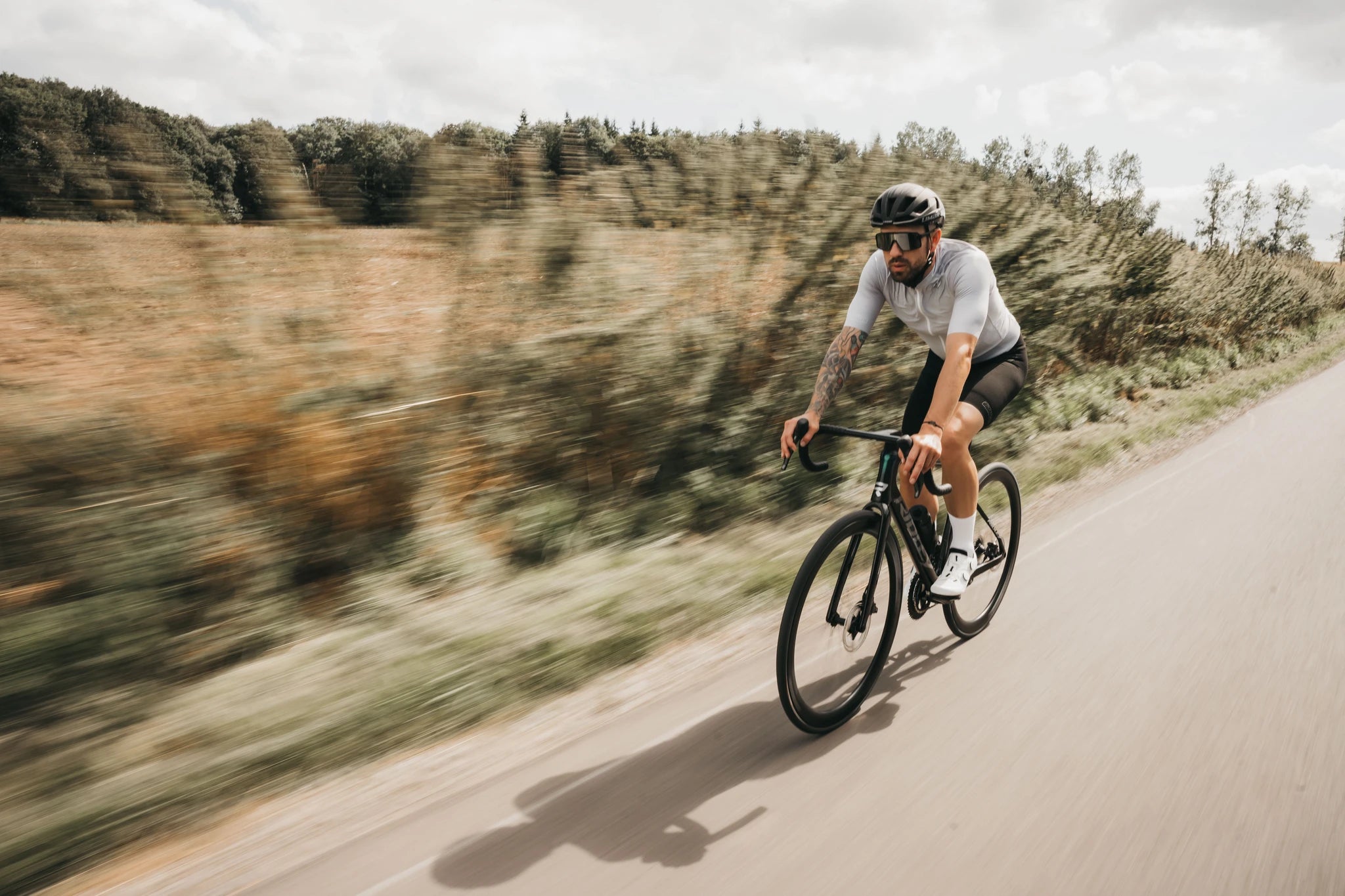 Radfahrer fährt auf einem Ridley-Rennrad schnell auf einer ländlichen Straße, trägt Helm und Sportkleidung.