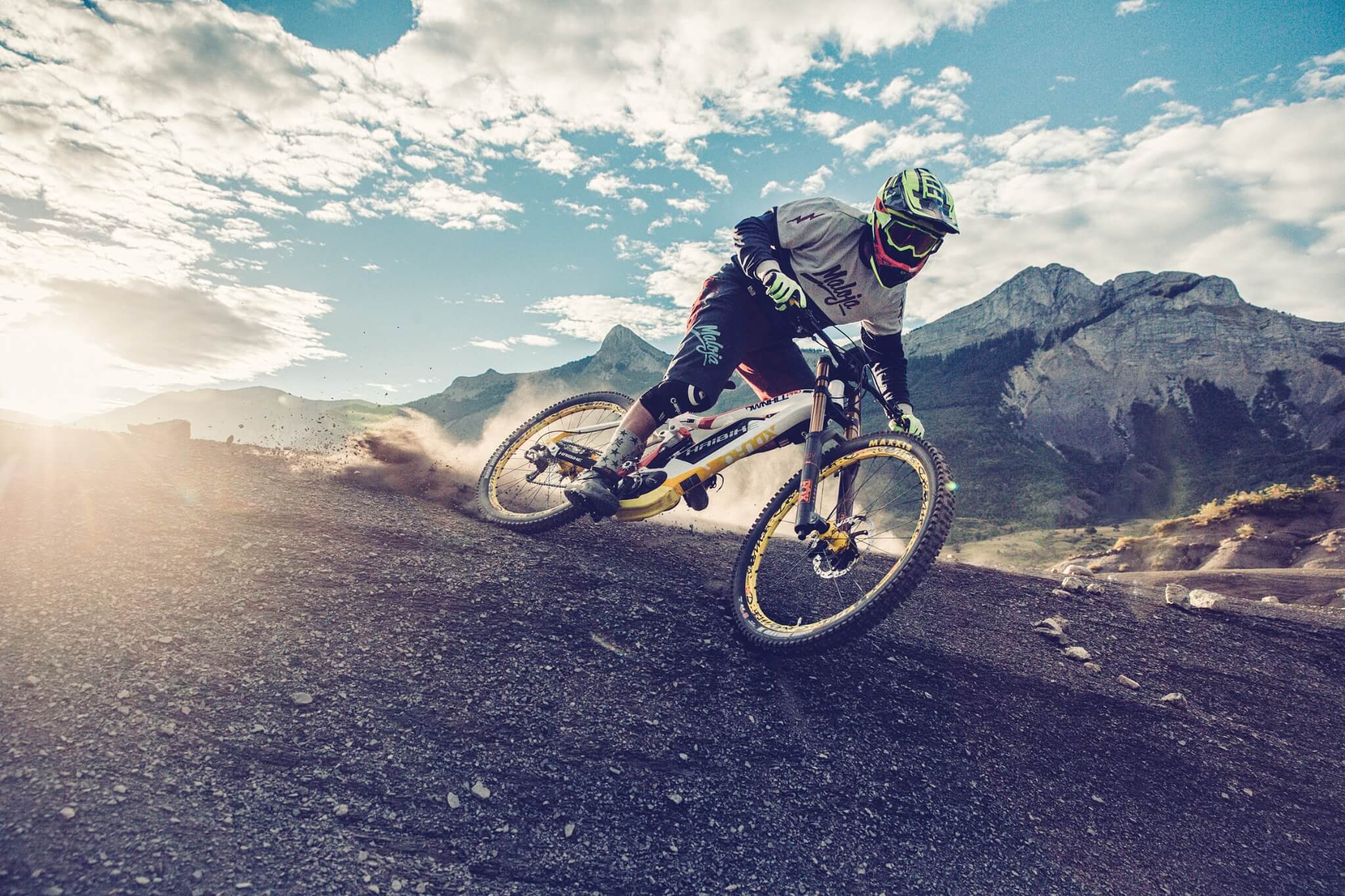 Mountainbiker auf Haibike-Fahrrad in Aktion, offroad auf Kies, vor Bergkulisse bei Sonnenschein, trägt Schutzausrüstung.