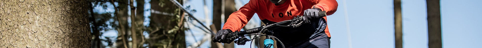 Person auf Fahrrad im Wald, trägt orangefarbenes ION-Shirt und Handschuhe.