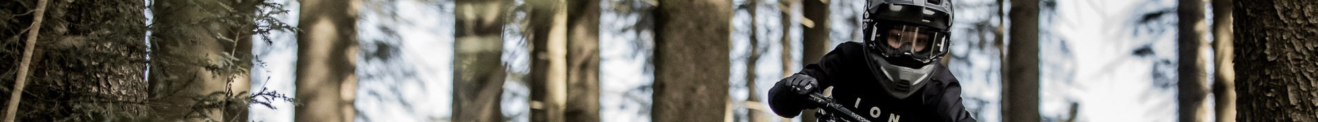 Ein Mountainbiker mit Helm und Schutzkleidung fährt durch einen Wald. Ideal für abenteuerliche Touren ab 10 Jahren.