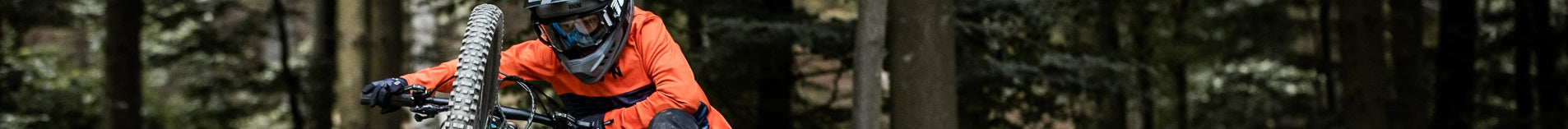 Person auf Mountainbike mit orangem Outfit und Helm fährt durch einen Waldweg.