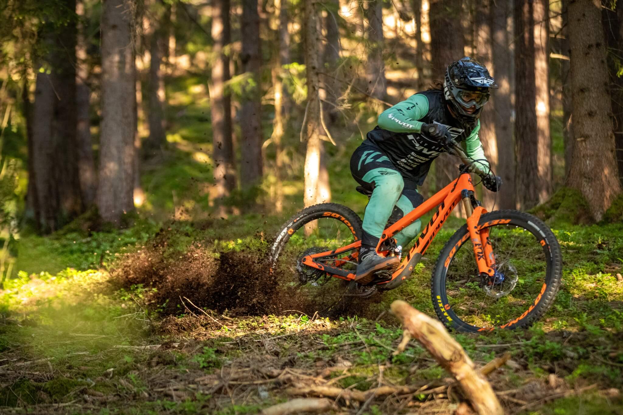 Mountainbiker auf orangefarbenem Pivot-Bike fährt durch Wald, aufgewirbelte Erde im Vordergrund, geeignet für Offroad-Fahrten.