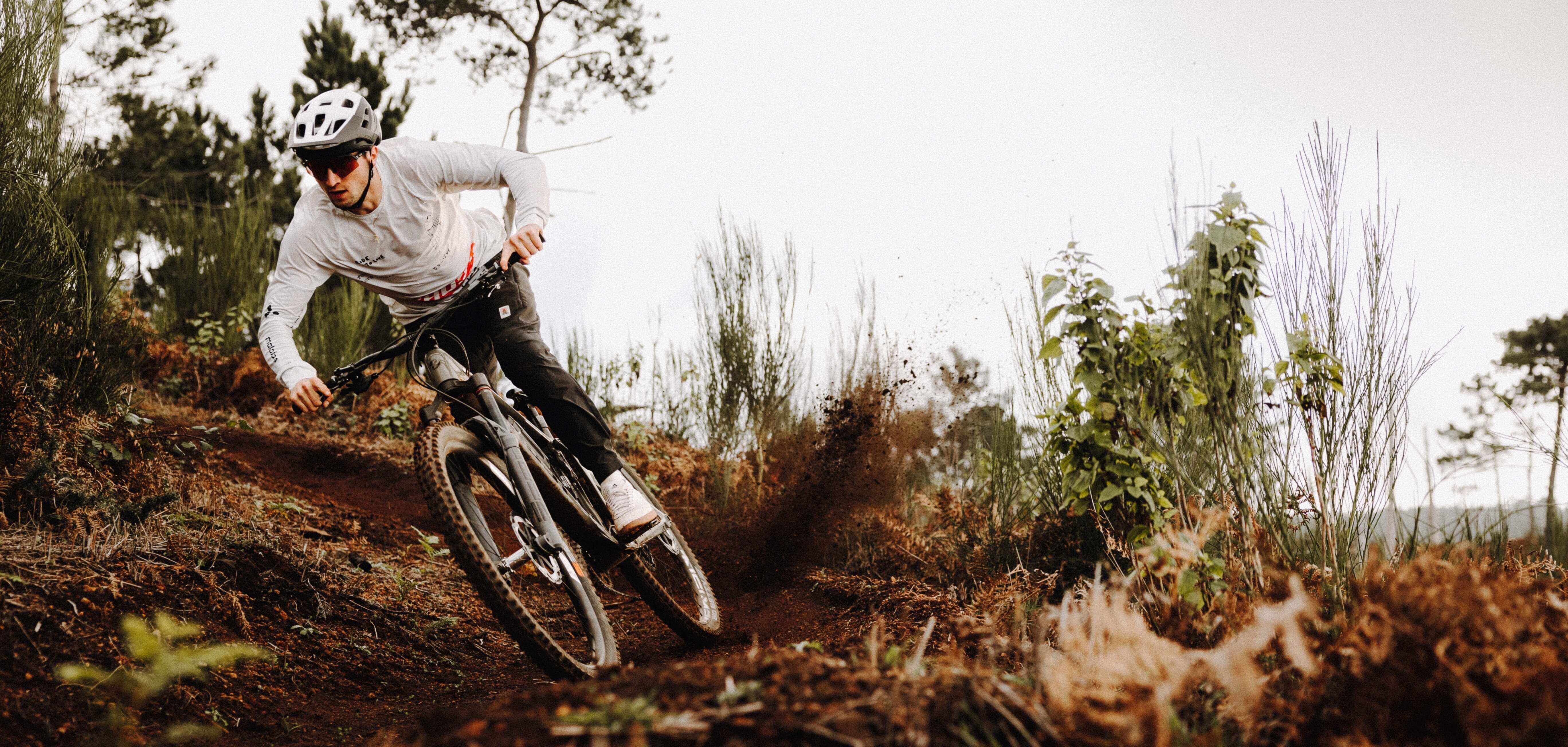 Mountainbiker in Aktion auf kurviger Waldstrecke mit Helm und Sportkleidung, wirbelnder Staub im Hintergrund.