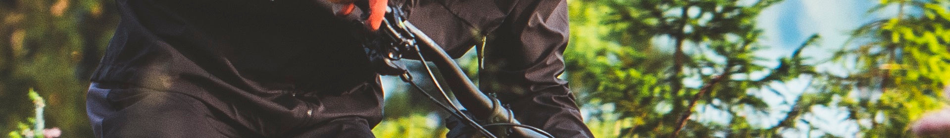 Person auf schwarzem Fahrrad in Bewegung, trägt schwarze Kleidung, im Hintergrund grüne Bäume; Haibike E-MTB Fully.
