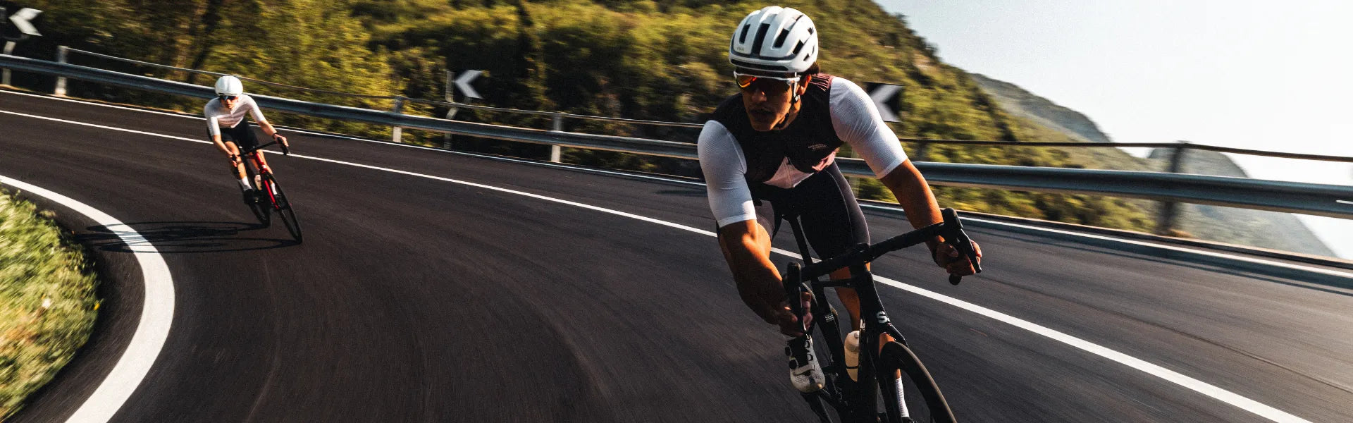 Zwei Superior Radfahrer in Rennkleidung fahren schnell eine kurvige Landstraße hinunter, umgeben von grüner Landschaft.