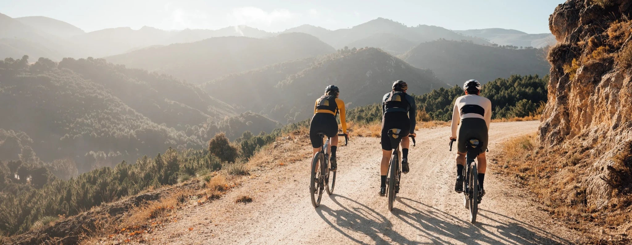 Drei Radfahrer auf Schotterweg in bergiger Landschaft. Perfekt für Gravelbiking und Outdoor-Enthusiasten.