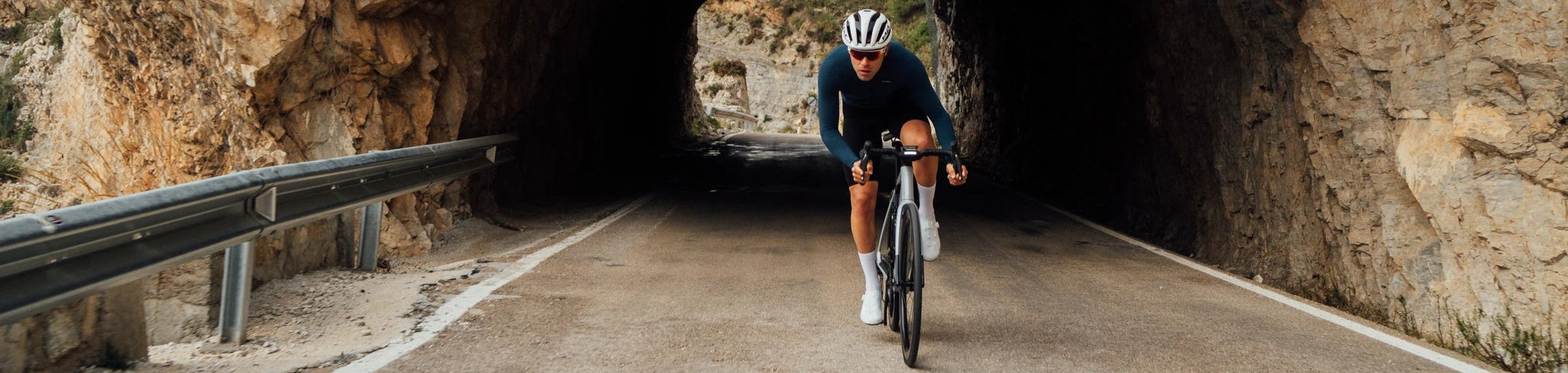 Radfahrer auf Orbea-Gain-Rennrad durchquert Tunnel in bergiger Landschaft bei Tageslicht.