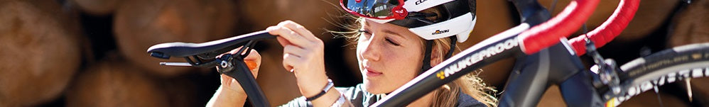Frau justiert Fahrradsattel von SQLab, trägt Fahrradhelm, im Hintergrund Brennholzstapel. Zielgruppe: Radfahrer.