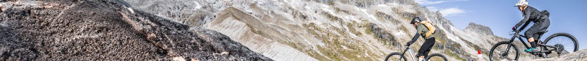 Zwei Mountainbiker fahren auf Specialized-Bikes über felsige Berglandschaft unter klarem Himmel.