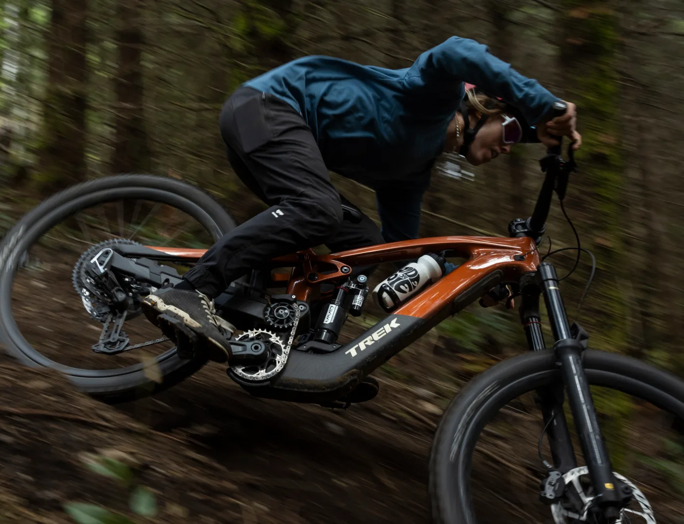 Person fährt ein braunes Trek Mountainbike im Wald, sportliche Kleidung, Fokus auf Geschwindigkeit und Manövrierfähigkeit.