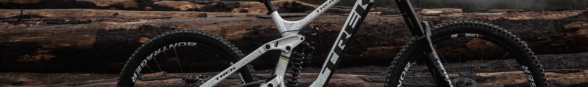 Graues Trek Mountainbike vor gestapelten Holzstämmen, geeignet für Offroad-Abenteuer und sportliche Fahrer.