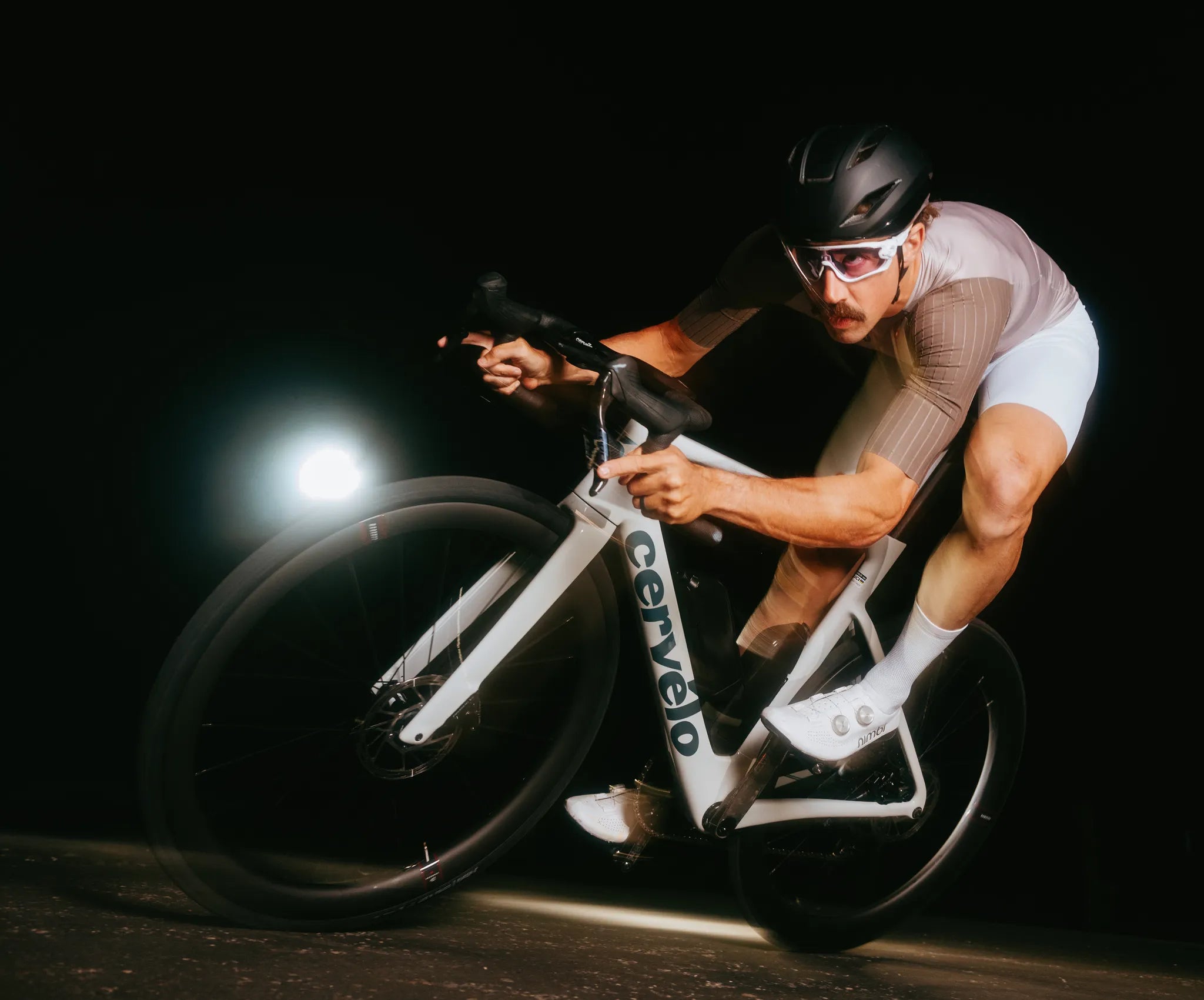 Radfahrer in sportlicher Haltung auf einem Cervélo-Rennrad bei Nacht, trägt Helm und Brille.
