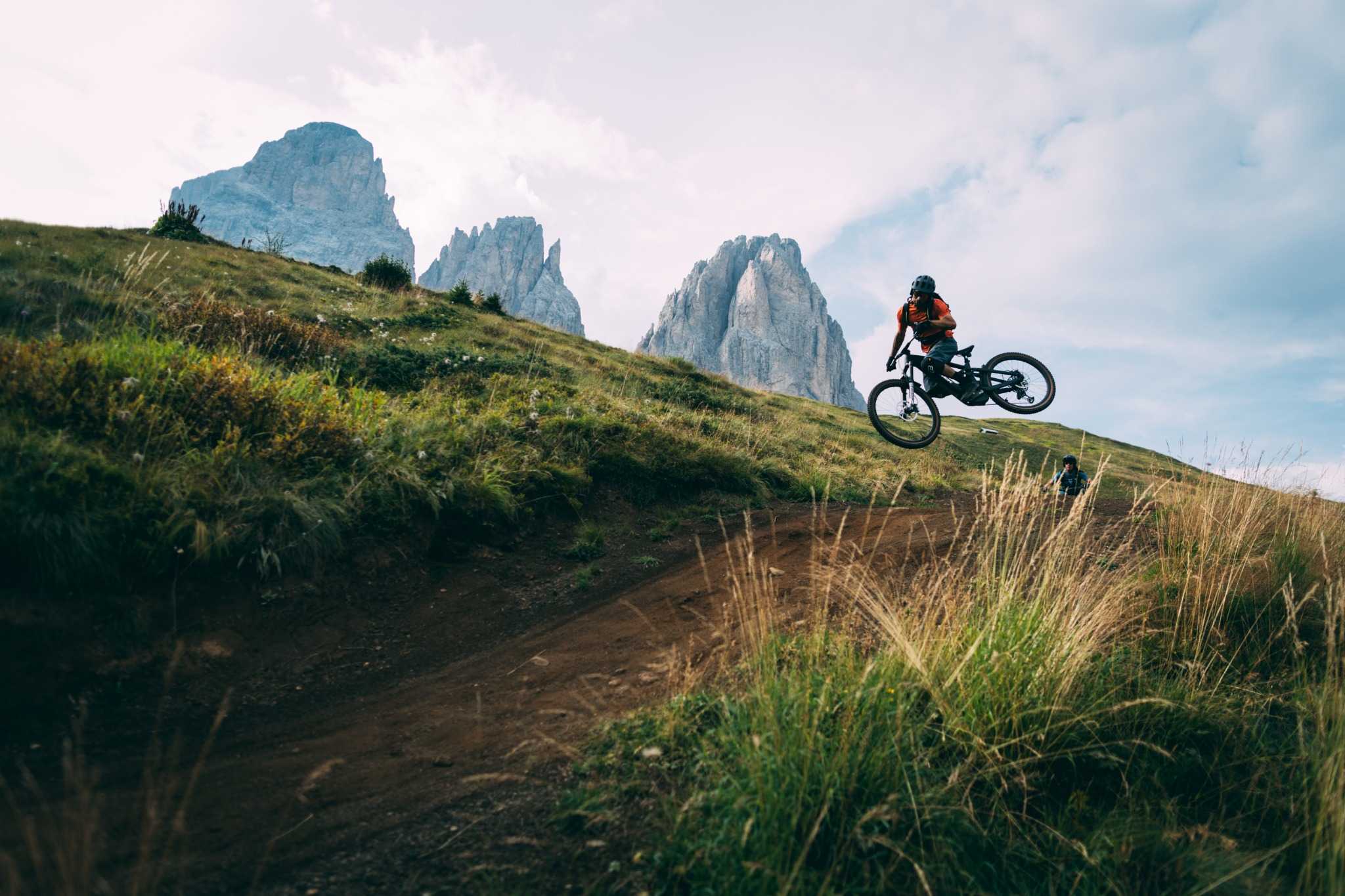 Mountainbiker springt mit E-Bike über Hügel in alpiner Landschaft. Ideal für Offroad-Fans. Modell: Trek Rail.