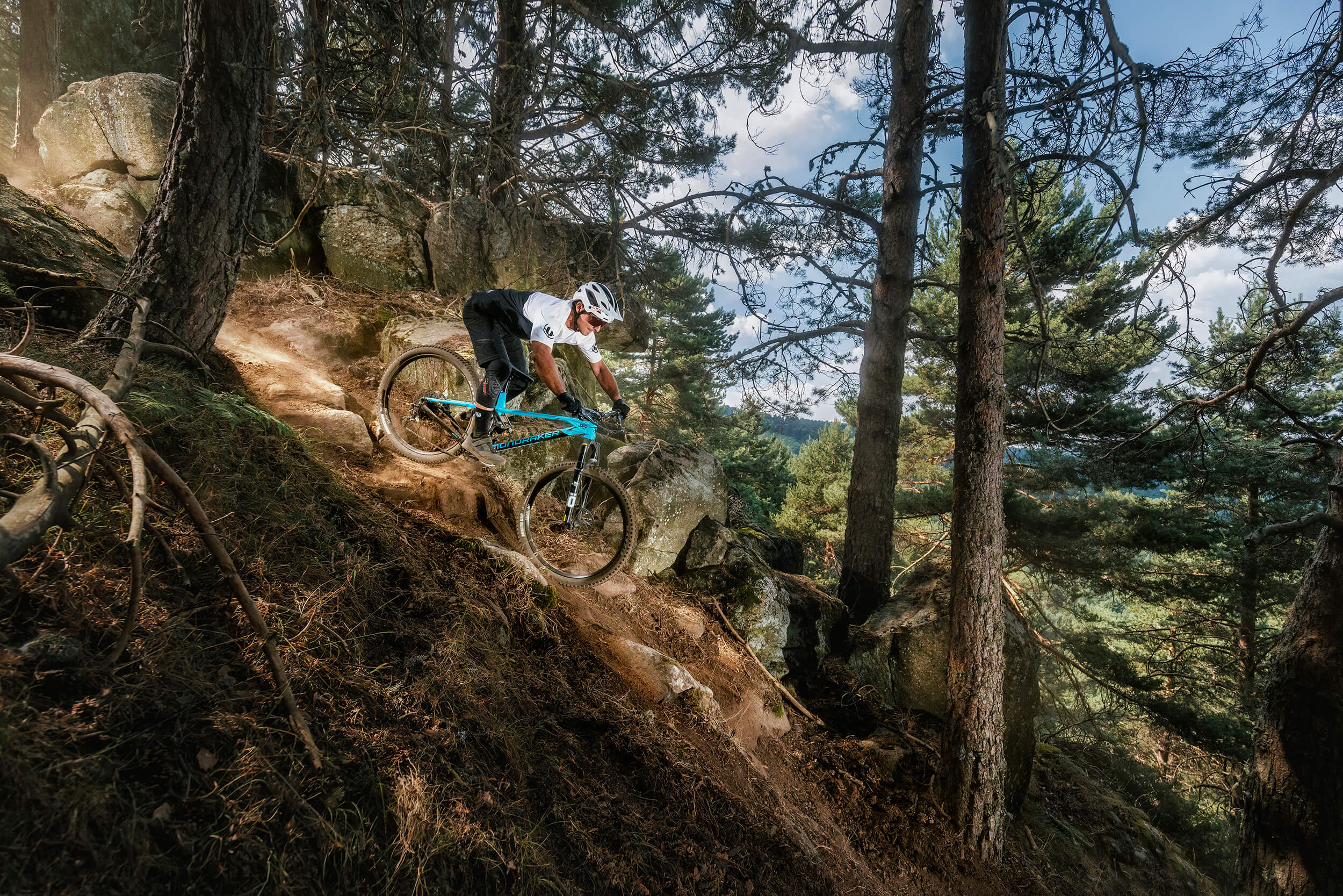 Mountainbiker auf Mondraker Foxy fährt steilen Waldpfad hinab. Abenteuer und Action im Gelände für Enthusiasten.