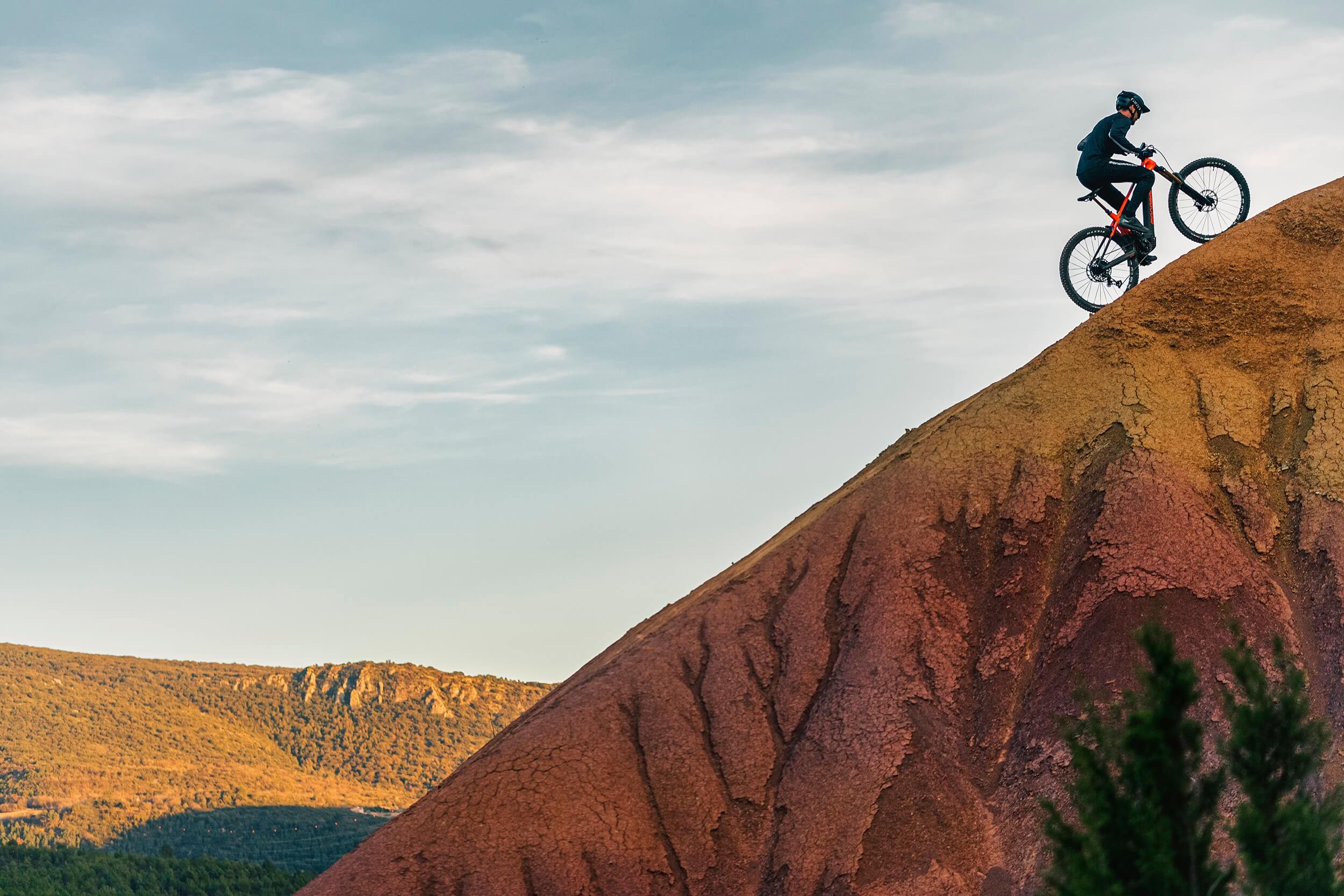 Person fährt ein Mondraker Prime E-Mountainbike einen steilen, roten Hügel hinauf unter blauem Himmel. Ideal für Offroad.