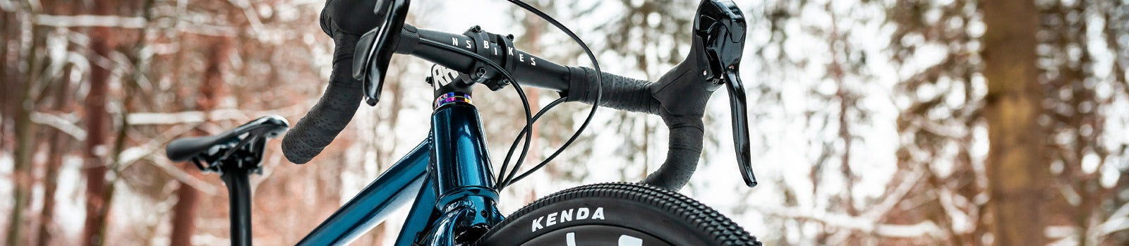 Gravelbike von NS Bikes im Wald, Nahaufnahme von Lenker und Reifen, geeignet für Offroad-Abenteuer.