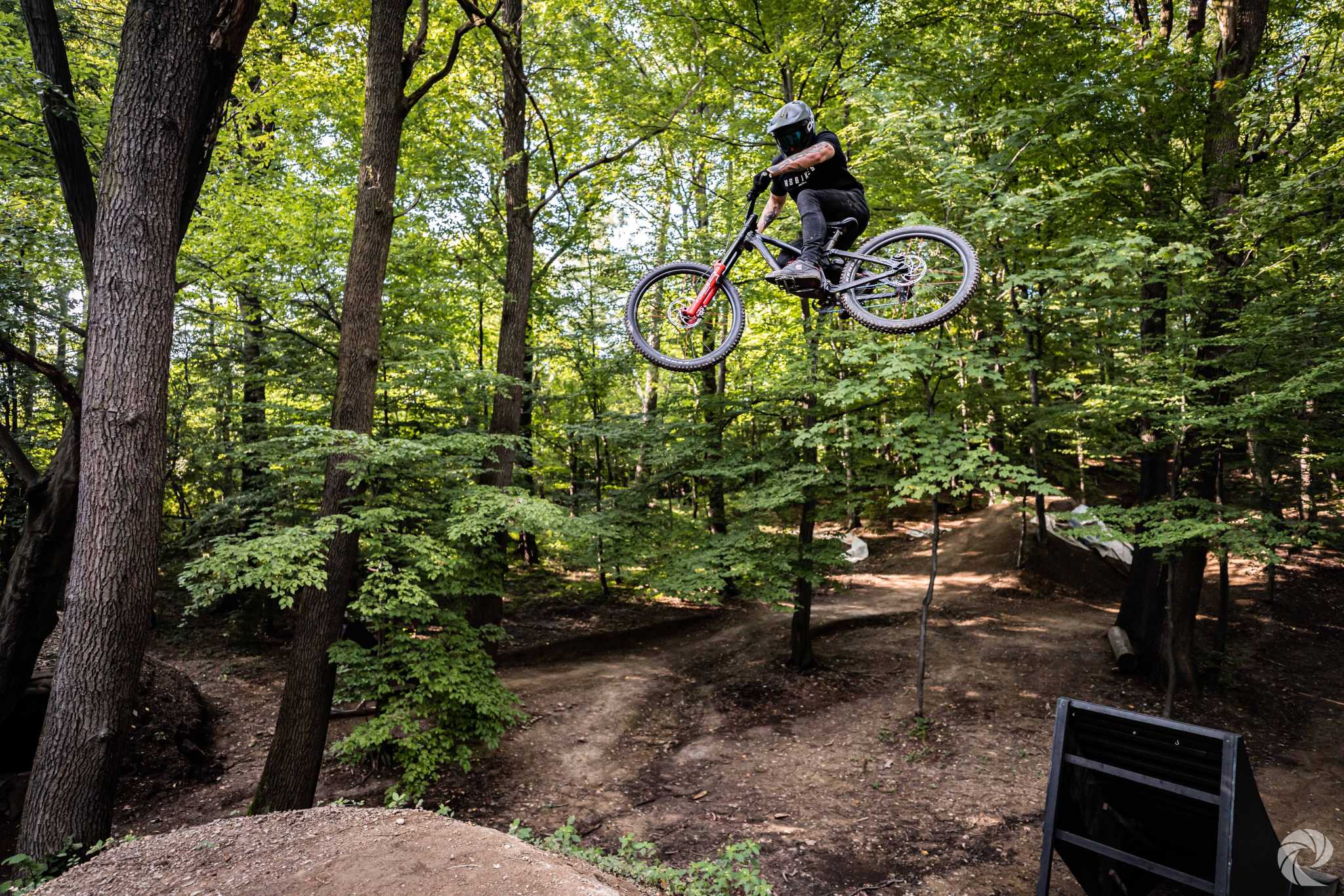 Person springt mit einem NS Bikes Mountainbike durch einen Wald, ideal für Downhill-Enthusiasten.