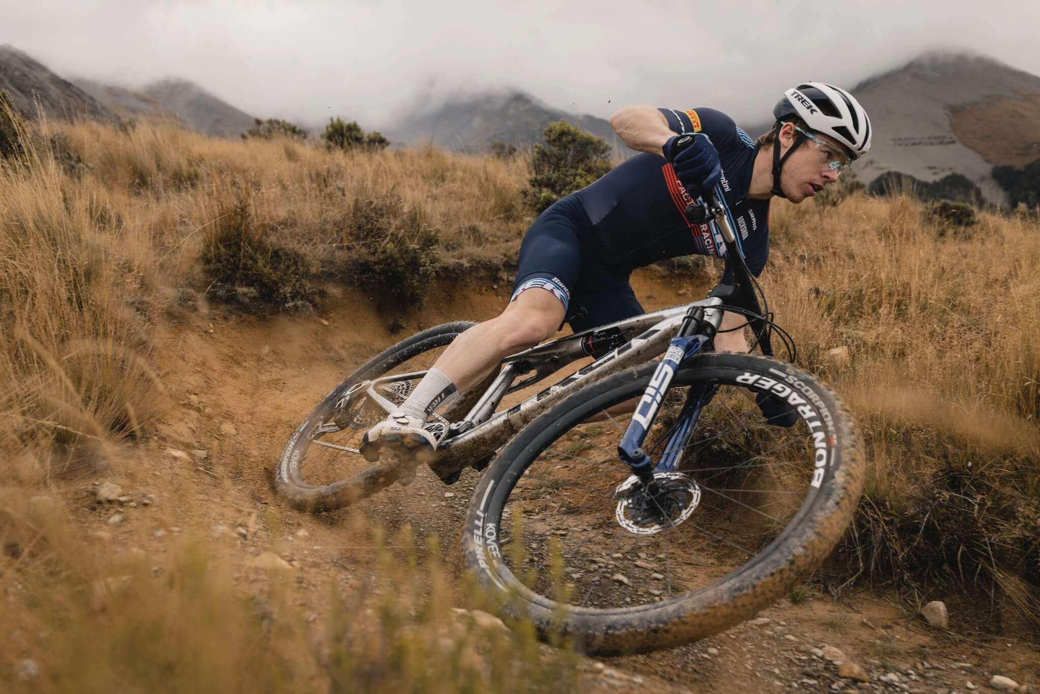 Radfahrer auf Trek Supercaliber Mountainbike in Aktion auf staubigem Trail in bergiger Landschaft.