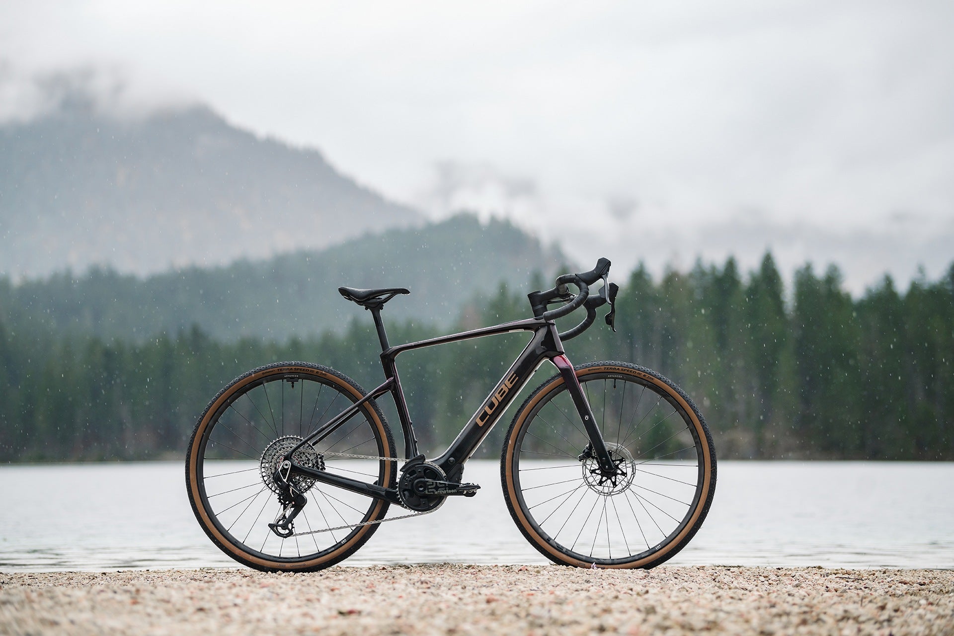 Cube Gravel Bike an einem Seeufer vor bewaldeten Bergen, ideal für Abenteuerfahrten in der Natur.