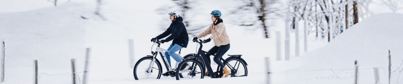 Zwei Personen fahren im Schnee auf E-Bikes von Gazelle, tragen Helme und Winterkleidung.