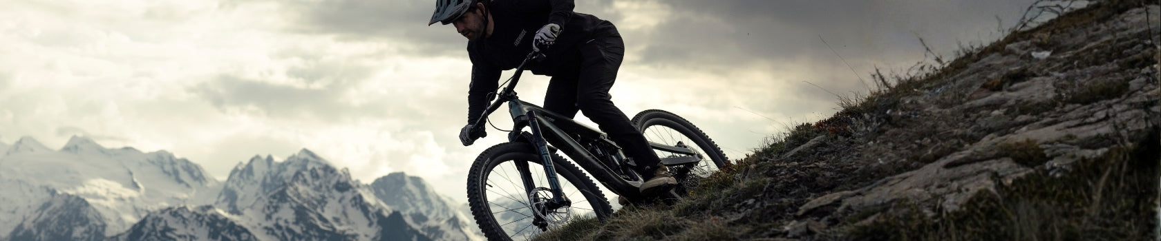 Mountainbiker auf einem Berghang, im Hintergrund schneebedeckte Gipfel. Geeignet für Outdoor- und Sportbegeisterte.