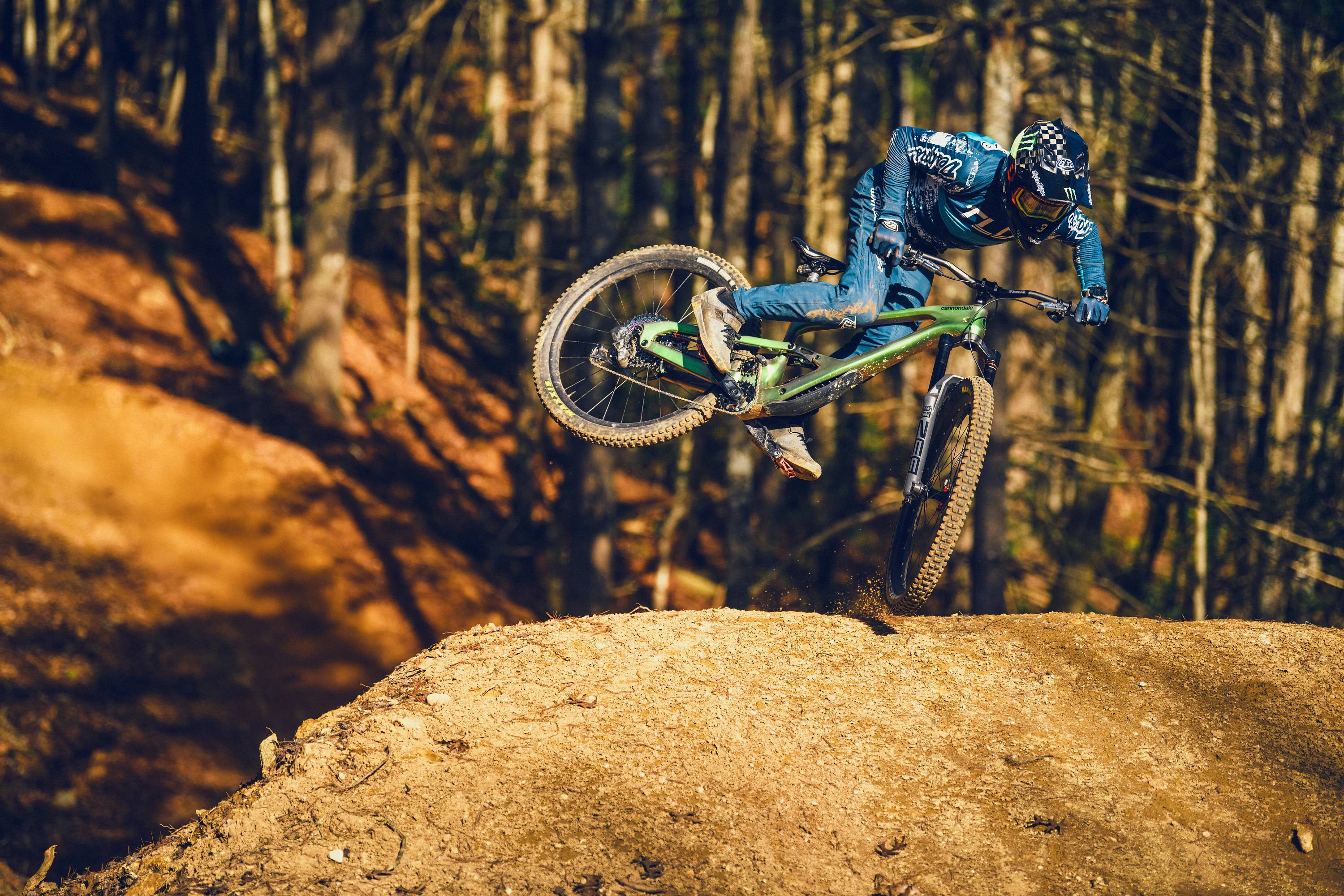 Mountainbiker springt mit Cannondale-Bike über Erdhügel im Wald, ideal für Offroad-Enthusiasten.