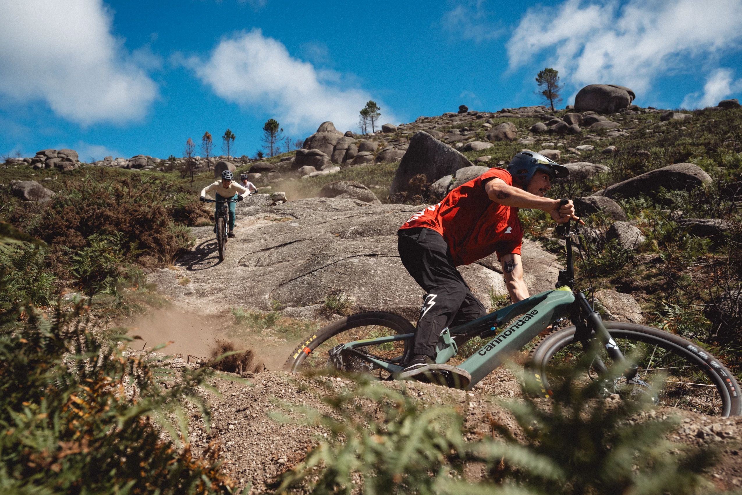 Zwei Mountainbiker fahren mit Cannondale-Bikes auf einem felsigen Trail in einer bergigen Landschaft.